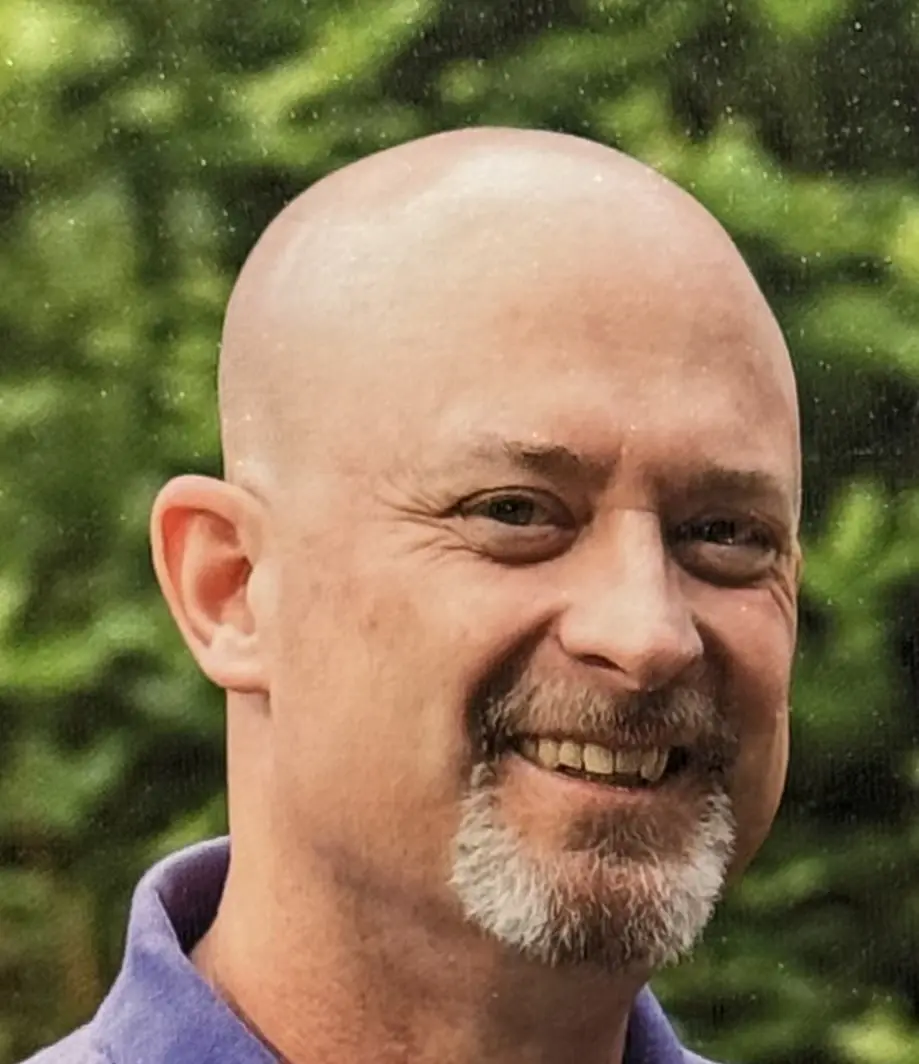 Smiling man outdoors with green background.