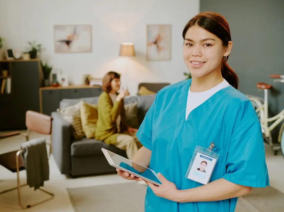 Smiling nurse holding tablet in living room.