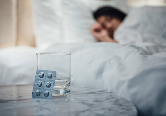 Pills and glass on bedside table, person sleeping.